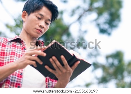 Man holding and reading the scriptures with a green tree background. Royalty-Free Stock Photo #2155163199