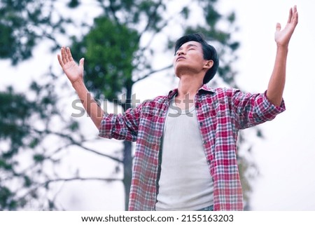 Man standing raised hands and praying to God with a green tree background. christian prayer concept.
