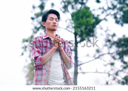 Man standing holding hands and praying to God with a green tree background. christian prayer concept.