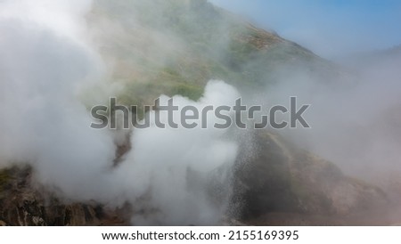 The hillside is shrouded in thick dense steam from an erupting geyser. Poor visibility. The blue sky is visible through the haze. Kamchatka. Valley of Geysers Royalty-Free Stock Photo #2155169395