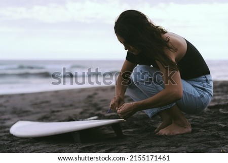Young woman surfer, preparing a surfboard on the ocean, waxing. Woman with safboard on the ocean, active lifestyle, water sports.