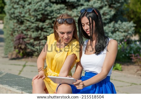 Cute girls sitting  outside and using the tablet computer