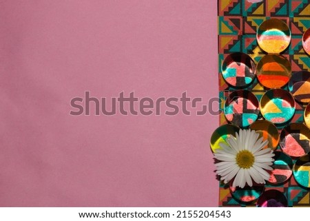 colorful retro wallpaper with transparent beads and daisy flower head next to the pink background as a copy space