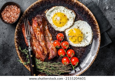 Breakfast with fried eggs and bacon with herbs in plate. Black background. Top view.