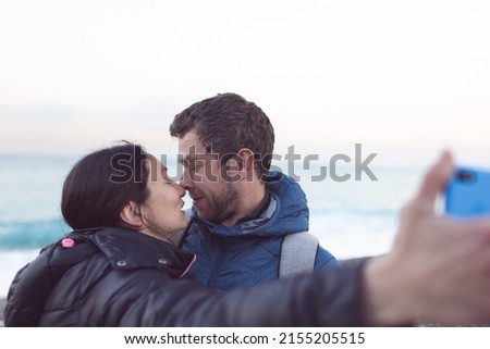 A man and a woman kiss on the beach, lovers take a selfie near the sea, two people hug