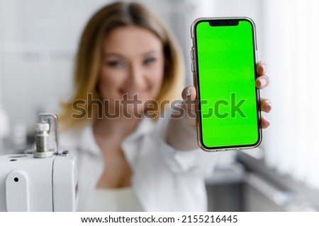 Young beautiful blonde hair worker in defocus holding a phone with a green screen on a light background.