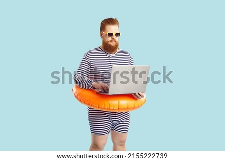 Funny man finds time for business during summer holiday at seaside. Serious chubby entrepreneur working on computer while on vacation. Busy plus size guy in striped swimsuit using his laptop at beach Royalty-Free Stock Photo #2155222739