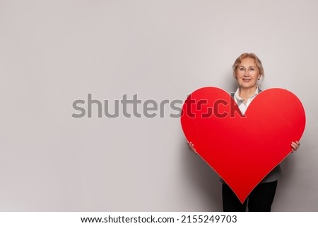 Happy senior woman holding big red heart banner on gray background