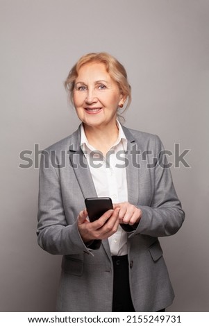 Portrait of happy senior businesswoman texting using smartphone on gray studio wall background