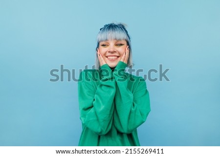 Joyful girl with blue hair stands on a green background with a smile on his face and happy looks away.