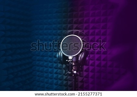 Microphone, headphones for singing, recording studio, black noise-cancelling walls, background, empty space for text, copy space. blue and purple light