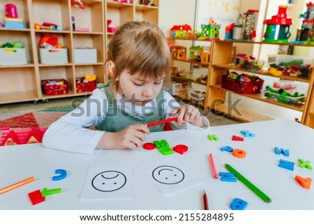 Little girl thinking about cards with different emotions at kindergarten or childcare centre. Selective focus.
