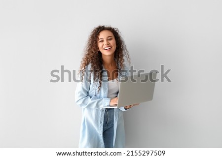 Happy young African-American woman using laptop on light background