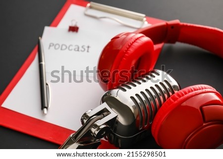 Modern microphone, headphones ad paper with word PODCAST on dark background, closeup