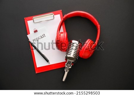 Microphone, headphones, clipboard and paper sheet with word PODCAST on dark background