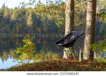 Beautiful forest lake with camping folding chair, book and vacuum insulated bottle. Royalty-Free Stock Photo #2155300245