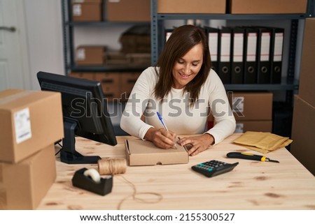 Middle age woman ecommerce business worker writing on package order at office