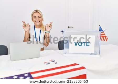 Young caucasian woman at america political campaign election gesturing finger crossed smiling with hope and eyes closed. luck and superstitious concept. 