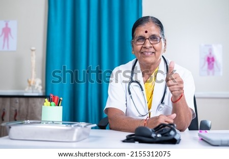 Happy senior woman doctor showing thumbs up by looking at camera at hospital with copy space - concept of successful, professional occupation and healthcare service.