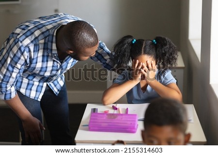 African american young male teacher consoling sad biracial elementary schoolgirl sitting at desk. unaltered, education, communication, childhood, sadness, depression, failure and school concept. Royalty-Free Stock Photo #2155314603