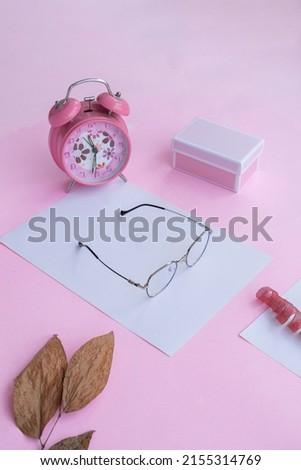 Product Presentation of Minimalist Concept Idea. square glasses, gift box, clock and dry leaves on pink paper background.
