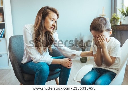 Psychologist touching shoulder of frustrated little boy while trying to help him. Young supported adoption counselor showing a drawing of house to sad pensive little boy waiting for new loving family