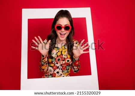 Photo of shiny impressed young lady dressed flower print outfit glasses standing inside photo frame isolated red color background