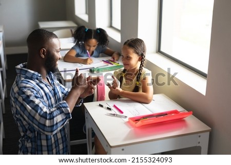 African american young male teacher communicating in sign language with caucasian elementary girl. unaltered, education, childhood, learning, teaching, disability and school concept.
