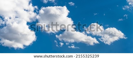 Sunlit white clouds on blue sky in abstract panoramic cloudscape background. Scenic panorama with beautiful group of fluffy cloud cumuli in summer clear air at hot sunny wheather. Nature conservation. Royalty-Free Stock Photo #2155325239