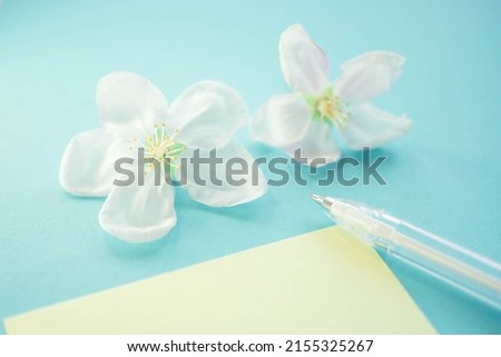 Two white blooming flowers, pen and blank paper on lovely blue table. Inspiration concept to create or write in spring mood
