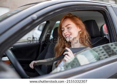 Young woman sitting on car seat and fastening seat belt, car safety concept. Woman fastens a seat belt in the car. Caucasian woman driver fastening car seat belt while sitting behind the wheel  Royalty-Free Stock Photo #2155332307