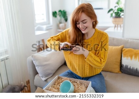 Young satisfied happy woman shopaholic customer sit on sofa unpack parcel delivery box, online shopping shipment concept. taking photos of product to post on social media
