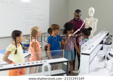 African american young male teacher showing skeleton to multiracial elementary students in lab. unaltered, education, childhood, learning, science, stem, teaching and school concept. Royalty-Free Stock Photo #2155345169