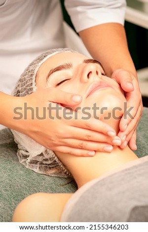 Facial treatment massage. Beautiful young caucasian woman with perfect skin receiving face and neck massage at a beauty spa