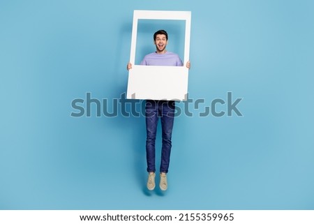 Full length body size view of attractive cheery guy jumping holding frame having fun isolated over bright blue color background
