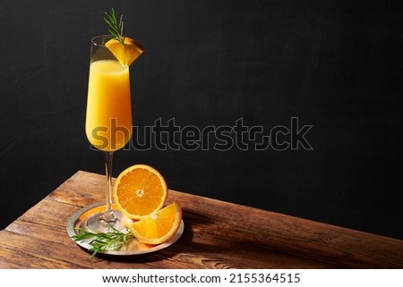 Mimosa cocktail in flute glass with orange slice and rosemary twig on a wooden bar and dark background. Horizontal photo with shallow depth of field and copyspace. Royalty-Free Stock Photo #2155364515