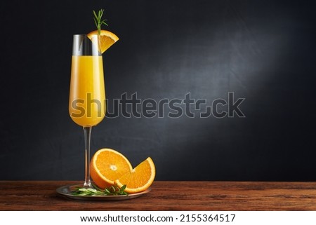Mimosa cocktail in flute glass with orange slice and rosemary twig on a wooden bar and dark background. Horizontal photo with shallow depth of field and copyspace. Royalty-Free Stock Photo #2155364517