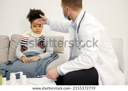 Male pediatrician holding hand on a forehead of sick little black girl