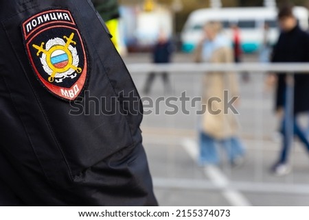 Close-up of chevron with emblem on uniform of the Russian police on the sleeve on a blurred background with fences and people. Translation: Police, MVD Royalty-Free Stock Photo #2155374073