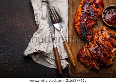Grilled turkey or chicken marinated fillet with red sauce served and sliced on wooden cutting board on stone brown background from above, poultry breast barbecue space for text Royalty-Free Stock Photo #2155379663