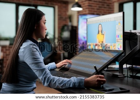Creative agency asian employee retouching digital photos while using touchscreen display and stylus pen. Professional picture retoucher with graphic tablet using editing software in office workspace.