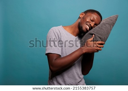 Happy man putting head on comfortable pillow to sleep and take nap in studio. Exhausted guy trying to get rest after passing bedtime and dealing with insomnia, sleeping schedule.