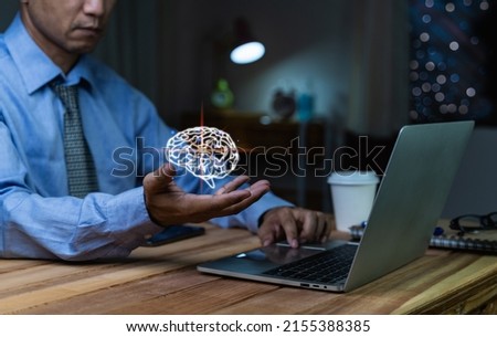 A businessman holding digital image of brain in palm, sitting at his desk by the window and using laptop in the office. business concept.