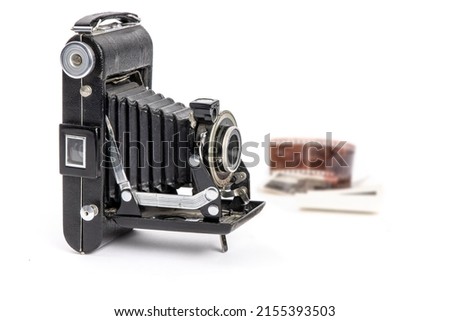 An antique old bellows camera with old film strip and photos in the background isolated on white