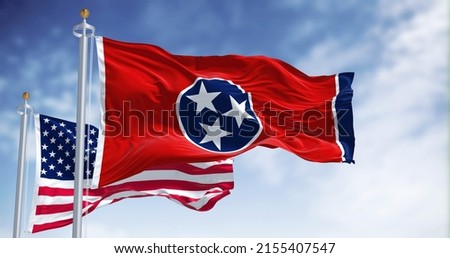 The Tennessee state flag waving along with the national flag of the United States of America. Tennessee is a state in the Southeastern region of the United States Royalty-Free Stock Photo #2155407547