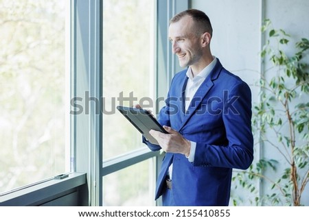 Young handsome businessman in a suit managing a business from a digital tablet Royalty-Free Stock Photo #2155410855