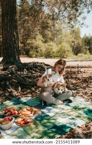 A young girl and her pet dog of the Welsh corgi Pembroke breed are relaxing on the beach and eating fruits, pastries and berries. The owner and the puppy have a good time on a picnic.