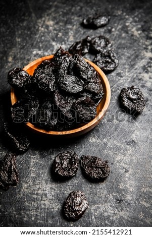 Prunes in a wooden plate on the table. On a black background. High quality photo