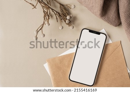Blank clipping path screen mobile phone with mockup copy space and dry floral branch and blanket cloth on neutral beige background. Minimal aesthetic business brand template. Flat lay, top view