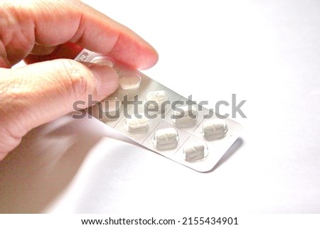 Man's hand picking up pills packed in a pack on a white background.
